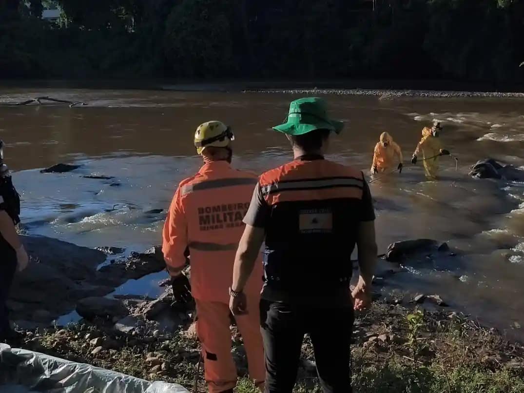Em Nova Era, equipes do Corpo de Bombeiros e da polícia acompanham uma operação de resgate em um trecho do Rio Piracicaba. Na imagem, militares uniformizados estão próximos às margens e dentro da água, entre rochas, realizando o trabalho de recuperação do corpo.