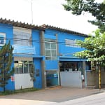 A imagem mostra a sede do Departamento de Águas e Esgotos (DAE) em um prédio de dois andares, pintado em tons de azul e branco. Na fachada, há o logotipo do DAE e uma placa com mensagem institucional sobre o uso consciente da água.