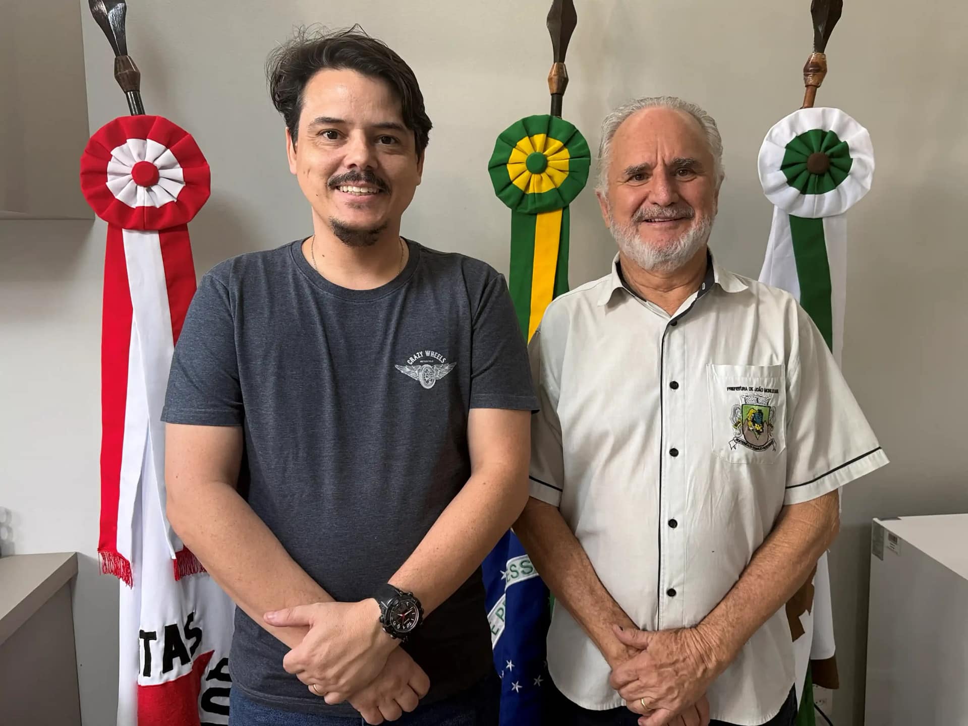 A imagem mostra dois homens em pé, lado a lado, posando para a foto em um ambiente interno institucional, possivelmente um gabinete público.