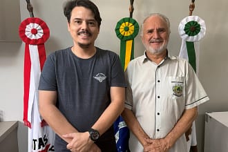 A imagem mostra dois homens em pé, lado a lado, posando para a foto em um ambiente interno institucional, possivelmente um gabinete público.