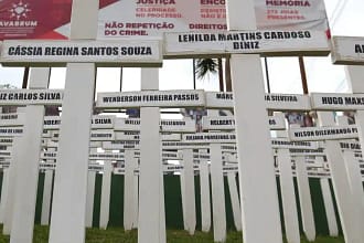 Imagem mostra um memorial composto por dezenas de cruzes brancas fincadas no chão, cada uma com o nome de uma das vítimas da tragédia de Brumadinho.