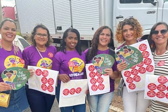A imagem mostra seis mulheres reunidas ao ar livre, sorrindo para a câmera e segurando materiais de campanha. Elas vestem camisetas roxas com ilustrações e mensagens de conscientização sobre a proteção de crianças e adolescentes. Cada uma segura folhas com vários adesivos vermelhos e leques informativos com o slogan “Pule, brinque e cuide”, relacionados à campanha de combate à exploração sexual infantil.