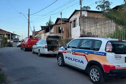 A foto mostra uma rua residencial com viaturas da Polícia Militar e do Corpo de Bombeiros estacionadas em fila ao longo da via. Em primeiro plano, aparece uma viatura da Polícia Militar de Minas Gerais, identificada com as cores branca, azul, vermelha e laranja. Logo à frente, há um veículo branco com o porta-malas aberto, seguido por uma viatura vermelha do Corpo de Bombeiros Militar.