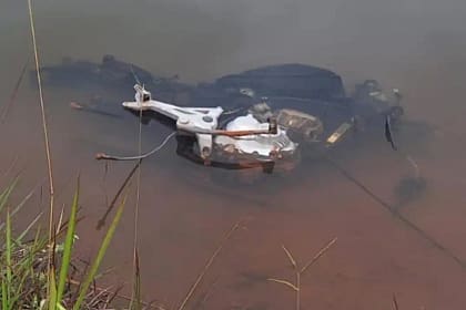 A imagem mostra uma motocicleta parcialmente submersa em uma lagoa, com a água de coloração turva e barrenta. Apenas parte da estrutura metálica do veículo permanece visível na superfície, destacando-se o motor exposto e componentes do chassi. A motocicleta aparenta estar sem rodas, carenagem e outras peças, indicando que foi desmontada ou “depenada” antes de ser abandonada no local.