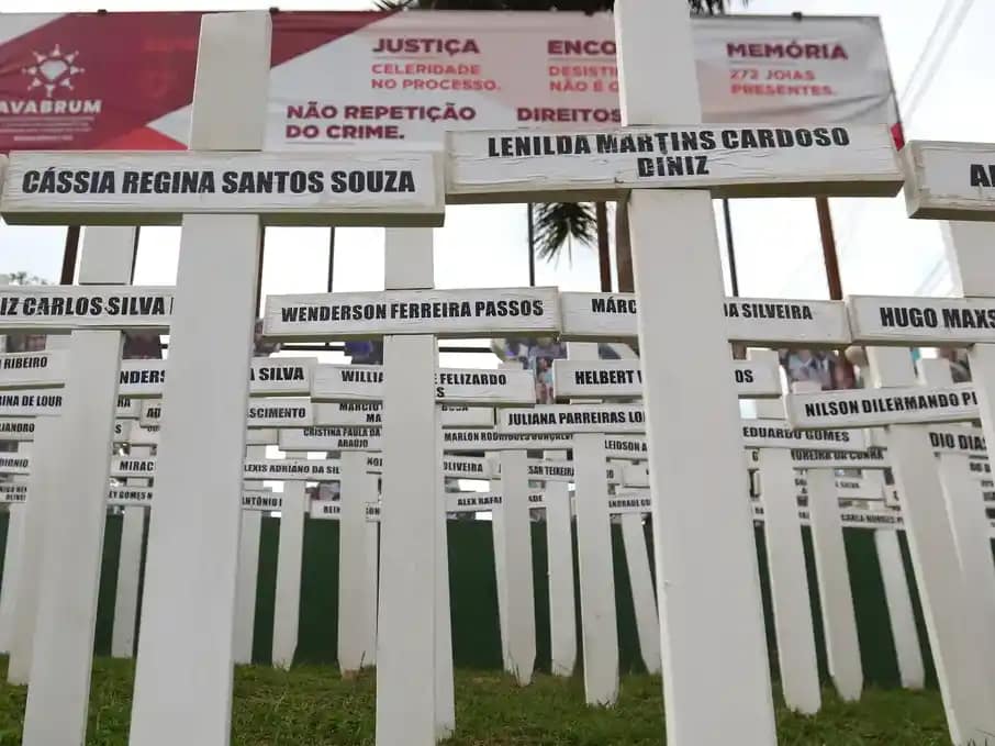 Imagem mostra um memorial composto por dezenas de cruzes brancas fincadas no chão, cada uma com o nome de uma das vítimas da tragédia de Brumadinho.