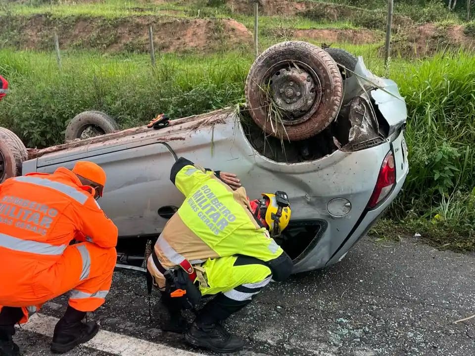 Bombeiros militares atuam no atendimento a um carro capotado na BR-262, em São Domingos do Prata. O veículo está virado de cabeça para baixo às margens da rodovia, enquanto os socorristas realizam procedimentos de segurança e avaliação no local, com vegetação ao redor da pista.